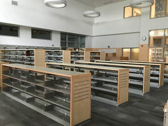 Rows of empty bookcases sit in the new library space. There are low cases and higher cases.
