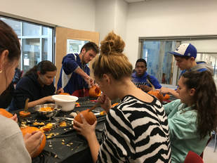 A group of students sits at tables carving pumpkins