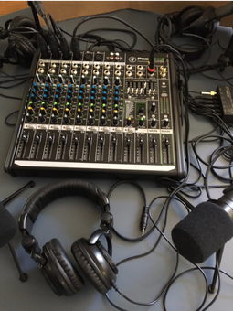 A sound mixing board is on a table with a microphone and headphones in front of it. 