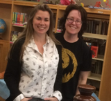 Two women standing in front of a chocolate fountain in a library. One is younger, with longer hair, and the other is wearing a dark t-shirt, and has shorter, dark hair.