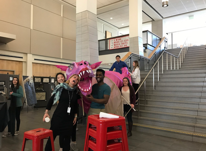 A group of students poses on stairs holding a ten foot long pink dragon puppet.