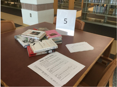 Three piles of books are on a table with a sign saying 