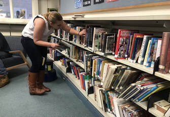 A female student works on shelving books. 