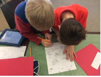 Two boys bend over their worksheets to work on their graphic novels. 